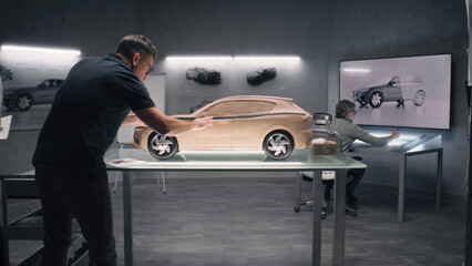 Two male automotive designers creating model of car in modern car design studio. One sculpting with plasticine clay, other working at the touch table. Future design of eco friendly electric car.