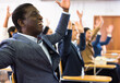 Excited african american man sitting with raised hands during group religious prayer meeting or motivational training in conference room