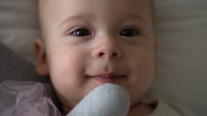 Close-up Happy playful kid 6 month old. Newborn boy looking at camera after bath shower on white soft bed. baby child waking time before bedtime with Toy. Childhood, motherhood, family, infant concept