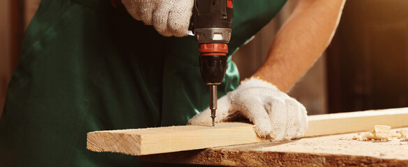 Professional carpenter twisting screw into wooden plank with drill in workshop, closeup. Banner design