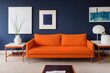 © The 2R Artificiality - Orange pillow and blanket on navy blue sofa in colorful living room interior with table. Real photo