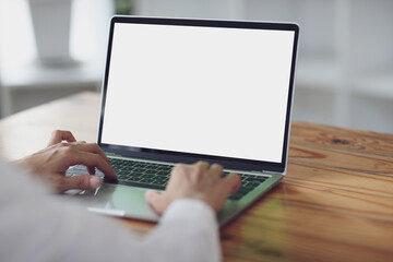 woman using and typing on laptop computer with blank white desktop screen on wooden table