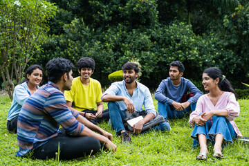 Group of happy students having chat with each other while sitting on college campus park - concept of takng break, communication and development.