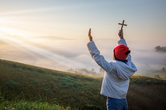 Child holding christian cross Prayer to God beautiful sunrise or sunset background.christian concept.