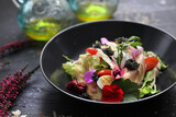 Fototapeta Kwiaty - Salad with vegetables, fresh fish, caviar and quail egg, decorated with edible flowers. Salad in a black bowl, close up.