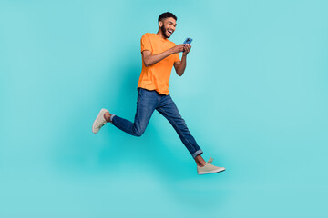 Wall Mural - Full length photo of good mood man dressed orange t-shirt typing apple modern device jumping high isolated turquoise color background