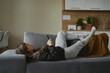 © gpointstudio - Caucasian woman lying down on the couch and using mobile phone