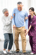 © Nassorn - Elderly man patient holding stick walking with support from senior woman and young nurse. Caregiver helps old man has illness recovery and standing at nursing home. Senior couple in rehabilitation.
