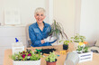 © Jelena Stanojkovic - Lovely senior housewife with flower in pot and gardening set indoors. Portrait of elderly woman gardening at home. Retired female care for her plants.