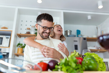 happy young couple have fun in modern kitchen indoor while preparing fresh fruits and vegetables food salad. Beautiful young couple talking and smiling while cooking healthy food in kitchen at home.