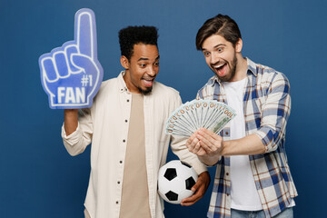 Wall Mural - Young two fan friends fun men wear white shirts foam glove finger up support football sport team with soccer ball watch tv live stream hold cash money isolated plain dark royal navy blue background.