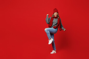 Wall Mural - Full body young woman wear grey sweater scarf hat do winner gesture celebrate clenching fists say yes isolated on plain red background Healthy lifestyle ill sick disease treatment cold season concept