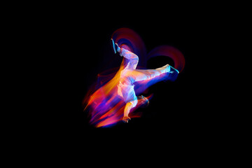 Dance in motion. Studio shot of flying, jumping dancer or gymnast performing tricks in the air over black background with mixed neon glowing rays