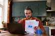 © ReeldealHD images - Young adult male at home looking at bills and personal finances using a laptop