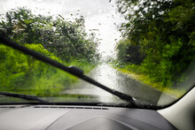 Driving in a low visibility on the country road caused by the heavy rain, view from car inside, focus at the rain drops on the windshield while the wipers is working