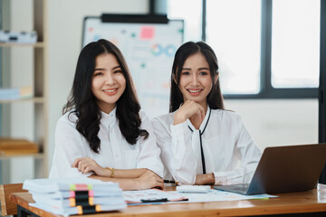 Portrait of beautiful asian businesswoman holding cup of coffee, smiling and looking at camera while sitting at office desk.