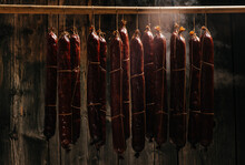Process Of Smoking Sausage Hang In A Cupboard With Smoke. Clouds Of Smoke Rise Up And Envelop The Sausages Hanging In A Row