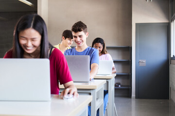 Wall Mural - Large Group of Multi Ethnic smiling Students Working on the Laptops while Listening to Lecture in the Classroom. Young cheerful People Study University. Selective focus in the guy. High quality photo