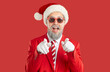 © Studio Romantic - Cheerful man in Santa hat is pointing his fingers at you, asking if you are ready for New Year party. Cool man in red jacket, sunglasses and with painted beard on red background. Christmas banner.