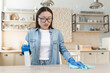 © Liubomir - Quarantine means. A young beautiful Asian woman disinfects the house, wipes the table with a cloth in blue rubber gloves, sprays the product. Bends from dirt and dust.