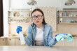 © Liubomir - Tired young beautiful Asian woman cleaning at home. Wipes the table with a rag in rubber gloves and a bottle of spray. He looks at the camera, spreads his hands.
