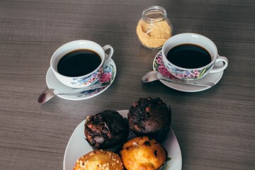 Canvas Print - Top view shot of two black teacups with muffins on a plate on a brown wooden table