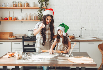 Wall Mural - happy cheerful mother and child in Santa Claus hats are cooking Christmas cookies in the kitchen. new year and Christmas