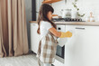 A cute little girl in an apron wipes the cupboard in the kitchen, washes with a sponge in a beautiful white kitchen with a window in a modern house. cleaning.