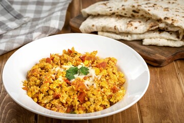 Wall Mural - Plate of scrambled eggs with tomatoes with lavash bread and a kitchen napkin on the background