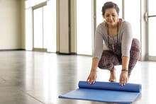 Woman Rolling Up Yoga Mat In Gym Studio