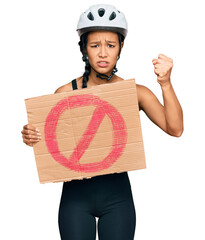 Poster - Beautiful hispanic woman wearing bike helmet and holding stop banner annoyed and frustrated shouting with anger, yelling crazy with anger and hand raised