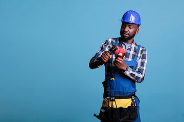 Wall Mural - Builder with drill and belt with all tools doing renovation for client, drilling holes in the wall or doing renovations. Professional builder in hard hat with tool belt on light blue background.