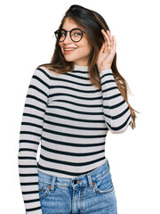 Poster - Young beautiful teen girl wearing casual clothes and glasses smiling with hand over ear listening an hearing to rumor or gossip. deafness concept.