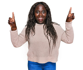 Poster - Young african woman wearing wool winter sweater smiling amazed and surprised and pointing up with fingers and raised arms.