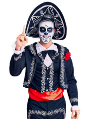 Canvas Print - Young man wearing day of the dead costume over background pointing finger up with successful idea. exited and happy. number one.