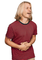 Poster - Caucasian man with blond long hair wearing casual striped t shirt with hand on stomach because nausea, painful disease feeling unwell. ache concept.