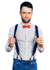 Poster - Hispanic man with beard wearing hipster look holding suspenders puffing cheeks with funny face. mouth inflated with air, catching air.