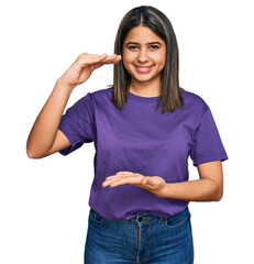 Sticker - Young hispanic girl wearing casual purple t shirt gesturing with hands showing big and large size sign, measure symbol. smiling looking at the camera. measuring concept.