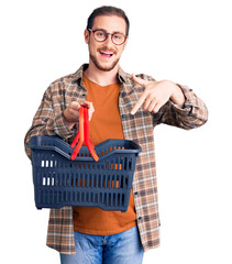 Wall Mural - Young handsome caucasian man holding supermarket shopping basket smiling happy pointing with hand and finger