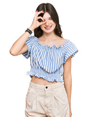 Canvas Print - Young beautiful caucasian girl wearing casual clothes doing ok gesture with hand smiling, eye looking through fingers with happy face.