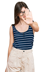 Sticker - Young beautiful caucasian girl wearing casual clothes and glasses doing stop sing with palm of the hand. warning expression with negative and serious gesture on the face.