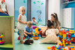 Caucasian preschoolers sitting on the floor with their teacher and enjoying numerous toys in kindergarten. High quality photo