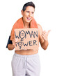 © Krakenimages.com - Young woman with short hair wearing sportswear holding woman power banner pointing thumb up to the side smiling happy with open mouth