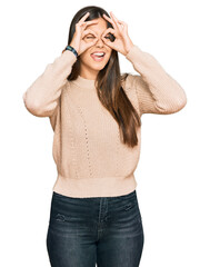 Wall Mural - Young brunette woman wearing casual winter sweater doing ok gesture like binoculars sticking tongue out, eyes looking through fingers. crazy expression.