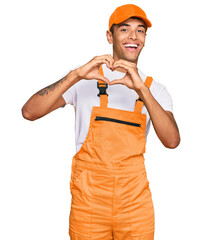 Sticker - Young handsome african american man wearing handyman uniform smiling in love doing heart symbol shape with hands. romantic concept.