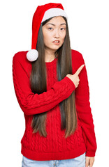 Wall Mural - Young chinese woman wearing christmas hat pointing aside worried and nervous with forefinger, concerned and surprised expression