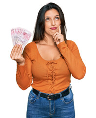 Poster - Beautiful hispanic woman holding 50 turkish lira banknotes serious face thinking about question with hand on chin, thoughtful about confusing idea