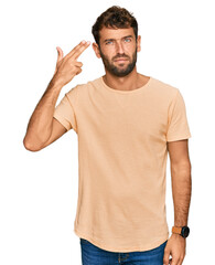 Poster - Handsome young man with beard wearing casual tshirt shooting and killing oneself pointing hand and fingers to head like gun, suicide gesture.