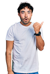 Sticker - Hispanic young man with beard wearing casual white t shirt surprised pointing with hand finger to the side, open mouth amazed expression.