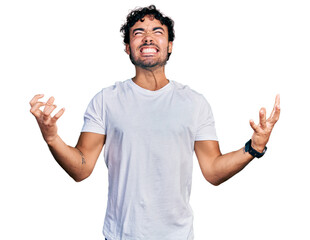 Canvas Print - Hispanic young man with beard wearing casual white t shirt crazy and mad shouting and yelling with aggressive expression and arms raised. frustration concept.